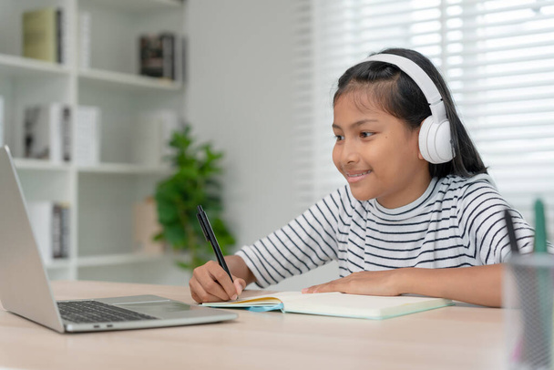 Online-Tutor Online-Kurs für asiatische Kinder. Videokonferenz am Laptop zu Hause. Online-Kurs abspielen, Schülerin trägt Kopfhörer zum Lernen, vermerkt Hausaufgaben, Videounterricht, neue Ausbildung. - Foto, Bild