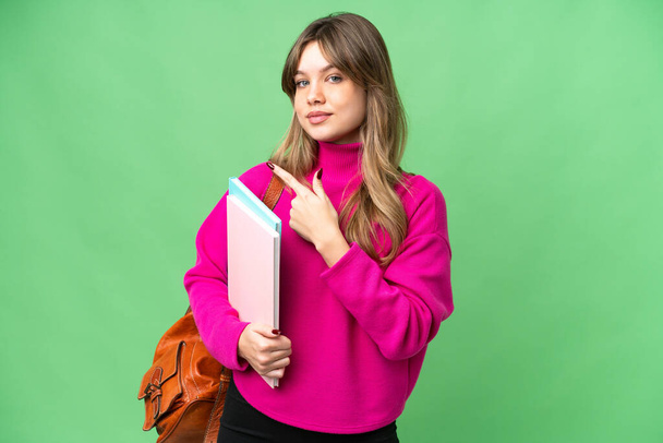 Молодая студентка с изолированным цветовым фоном указывает на сторону, чтобы представить продукт - Фото, изображение