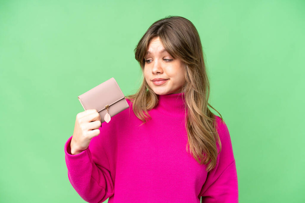 Young girl holding a wallet over isolated chroma key background with sad expression - Foto, afbeelding