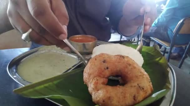 Κοντινό πλάνο του ανθρώπου τρώει αδρά και vada τοποθετείται πάνω από το φύλλο banyan σε plate.South ινδική συνταγή πρωινό Idly ή Idli κέικ ρυζιού σερβίρεται με καρύδα chutney και sambar - Πλάνα, βίντεο