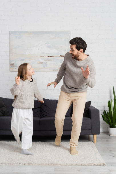 volle Länge der aufgeregten Mann mit preteen Tochter schauen einander beim Tanzen im Wohnzimmer - Foto, Bild
