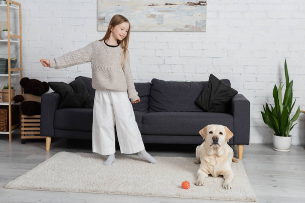 повна довжина радісної дитини, що грає з собакою-лабрадором на килимі у вітальні
  - Фото, зображення