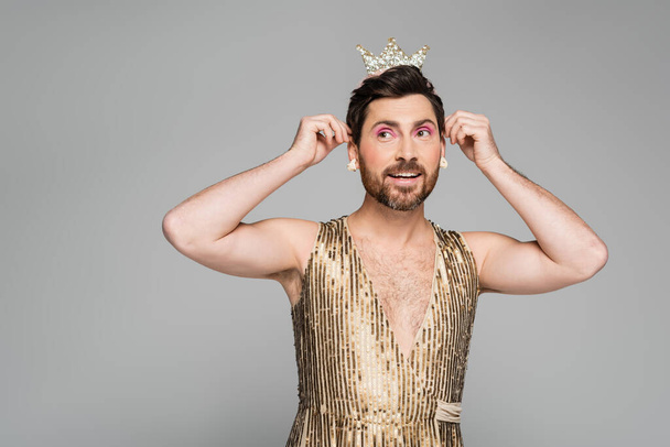 hombre alegre con corona de juguete en la cabeza mientras está de pie en traje de vestido de princesa aislado en gris  - Foto, imagen