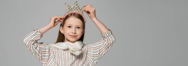happy girl adjusting crown on head and smiling isolated on grey, banner  - Foto, afbeelding
