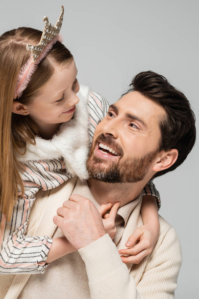 niño feliz en corona abrazando padre positivo con barba aislada en gris  - Foto, imagen