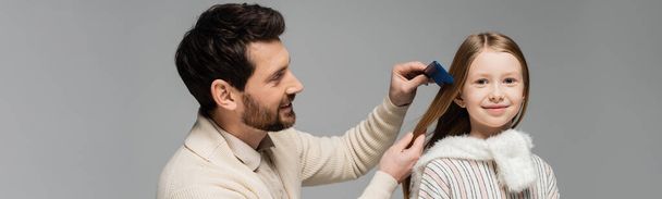 happy bearded father brushing hair of smiling daughter isolated on grey, banner  - Fotó, kép