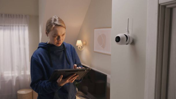 Caucasian woman installs security camera. Woman sets up angle of CCTV camera at home and rotates it with digital tablet computer and application. Concept of monitoring system, safety and privacy. - Fotografie, Obrázek