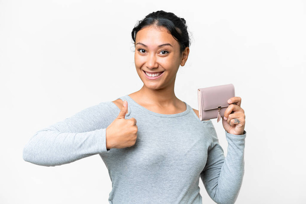 Young Uruguayan woman holding a wallet over isolated white background with thumbs up because something good has happened - Photo, image
