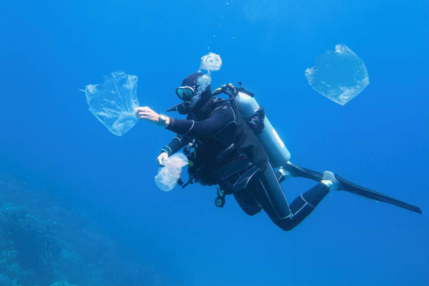 Mies sukeltaja puhdistaa muovia saastuneessa meressä. Maailman valtameri saastunut muovi. - Valokuva, kuva