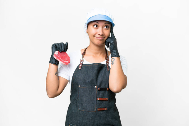 Butcher woman wearing an apron and serving fresh cut meat over isolated white background having doubts and thinking - Photo, image