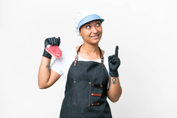 Boucher femme portant un tablier et servant de la viande fraîche coupée sur fond blanc isolé pointant vers le haut d'une excellente idée - Photo, image
