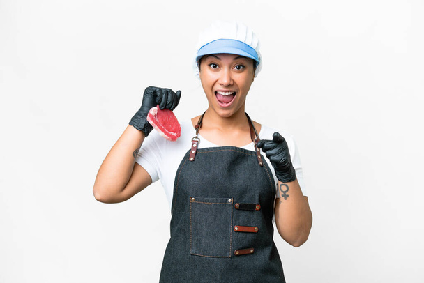 Butcher woman wearing an apron and serving fresh cut meat over isolated white background surprised and pointing front - Photo, image