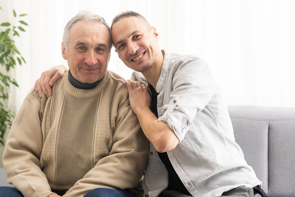 Young adult caucasian son listening and supporting his old elderly senior father at home indoors. Care and love concept - Foto, Bild