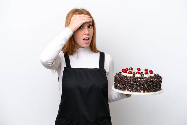 若いですredhead女性保持誕生日ケーキ隔離上のホワイトバック行います驚きジェスチャーしながら見ますザ · 側 - 写真・画像