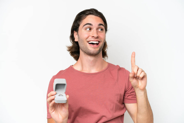 Young handsome man holding a engagement ring isolated on white background intending to realizes the solution while lifting a finger up - Photo, Image