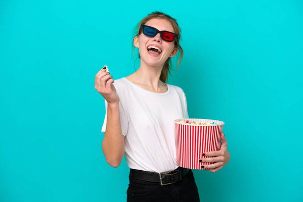 Young English woman isolated on blue background with 3d glasses and holding a big bucket of popcorns - Foto, Imagem