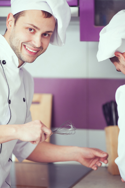 Retrato de un chef masculino sonriente con su compañero de trabajo cocinando comida a
 - Foto, imagen