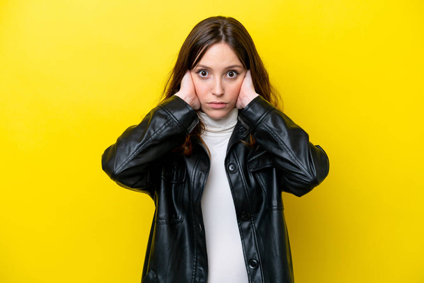 Молодая белая женщина, изолированная на желтом фоне, разочарованная и закрывающая уши - Фото, изображение
