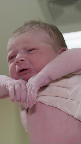 Vertikales Video. Eine Ärztin in weißen Handschuhen hält ein neugeborenes, weinendes Baby. Klinische Geburtsstation. - Filmmaterial, Video