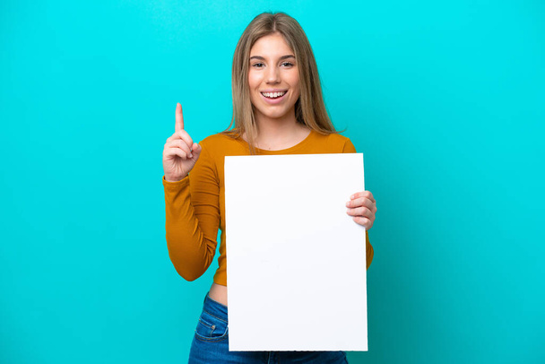 Young caucasian woman isolated on blue background holding an empty placard and pointing up - Photo, Image