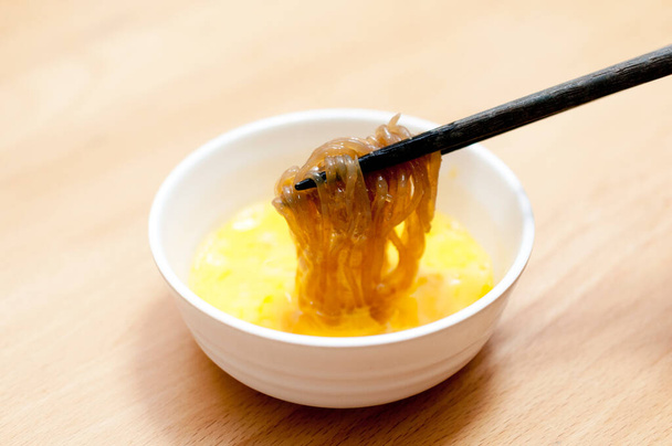 Sweet and spicy boiled Konjac noodles is dipped into a raw egg. - Foto, immagini