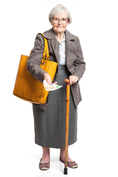 Mujer mayor sosteniendo dinero mientras está de pie sobre fondo blanco
 - Foto, imagen