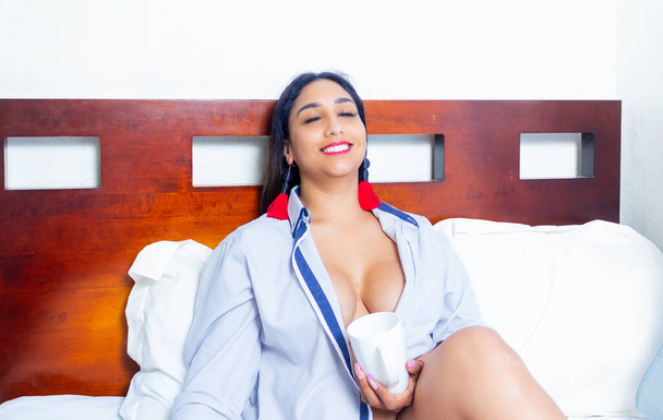 sexy latin woman sitting on bed with cup of coffee - Foto, afbeelding