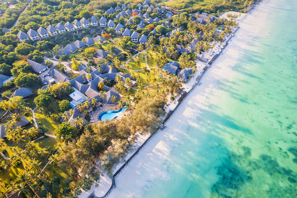 Top view of a tropical landscape in Zanzibar, Africa, featuring white sandy beaches, blue ocean waves, palm trees, and parasols. The aerial view captures the picturesque scene at sunset, creating the perfect setting for a summer holiday - Fotó, kép