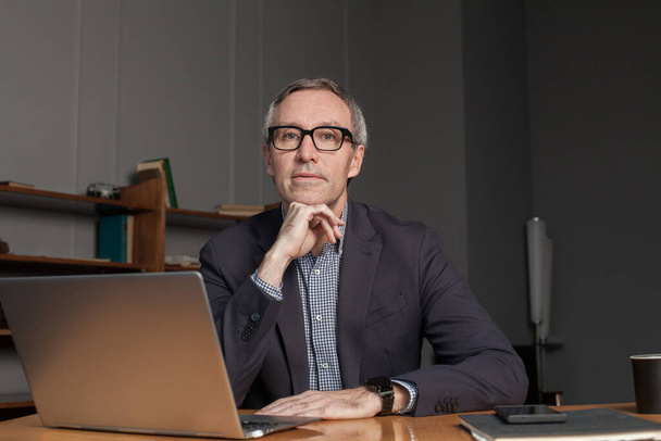 Mature businessman in eye glasses and suit is thinking about work with laptop - Photo, Image