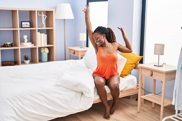 Afrikalı Amerikalı bir kadın yatak odasında kollarını açarak uyanıyor. - Fotoğraf, Görsel