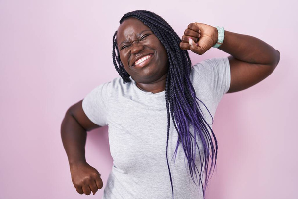 Young african woman standing over pink background stretching back, tired and relaxed, sleepy and yawning for early morning  - 写真・画像