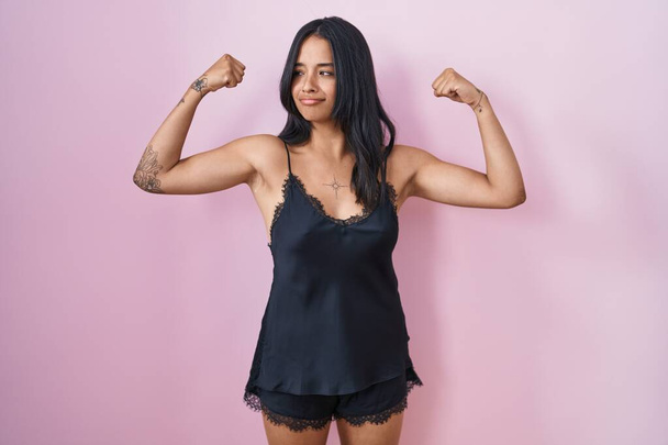 Siyah pijama giyen esmer kadın gururla gülümseyen kol kaslarını gösteriyor. fitness konsepti.  - Fotoğraf, Görsel