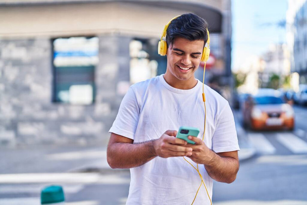 Giovane uomo ispanico sorridente fiducioso ascoltare musica in strada - Foto, immagini