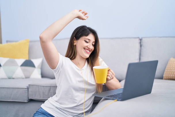 Young hispanic woman drinking coffee listening to music at home - Photo, image