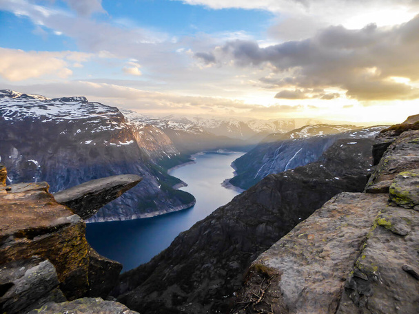 Famous rock formation, Trolltunga with a view from the above on Ringedalsvatnet lake, Norway. Rock hanging. Slopes of the mountains are partially covered with snow. Soft colors of the sunrise - Foto, afbeelding
