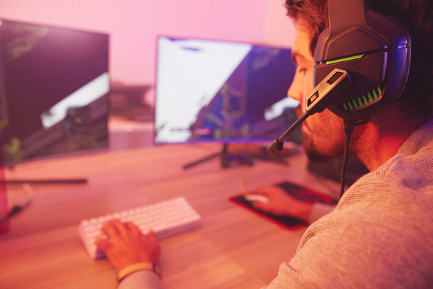 Computer gaming, man and esports player with headphones, video games and virtual competition in dark. Gamer guy, online challenge and headset of live streaming in neon lighting, tech and rpg streamer. - 写真・画像