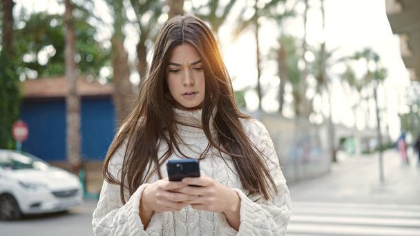 Young beautiful hispanic woman using smartphone with serious expression at street - Fotó, kép