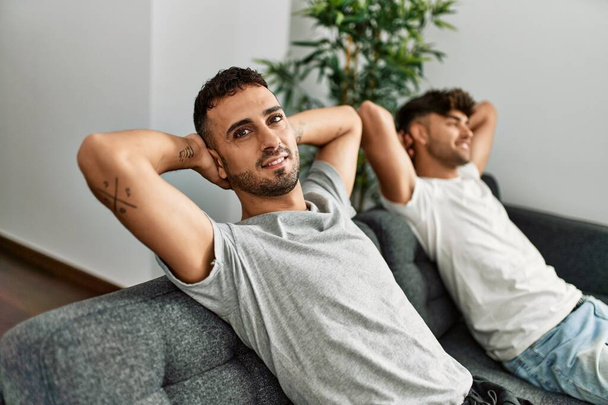Dois homens hispânicos casal sorrindo confiante relaxado com as mãos na cabeça em casa - Foto, Imagem