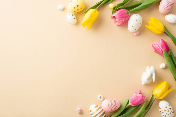 Concepto de decoraciones de Pascua. Foto vista superior de huevos de Pascua coloridos conejito de Pascua de cerámica y tulipanes sobre fondo beige claro aislado con espacio vacío - Foto, Imagen