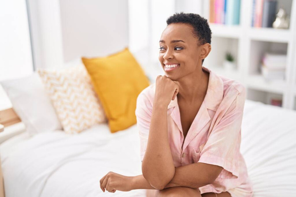 Африканська жінка - американка, яка впевнено посміхається, сидячи на ліжку у спальні. - Фото, зображення