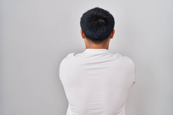 Junger Chinese steht auf weißem Hintergrund und blickt rückwärts mit verschränkten Armen weg  - Foto, Bild