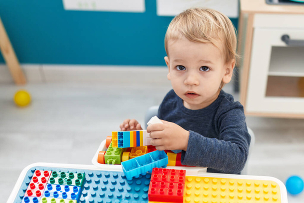 Adorable blond toddler playing with construction blocks sitting on table at kindergarten - Foto, Imagem