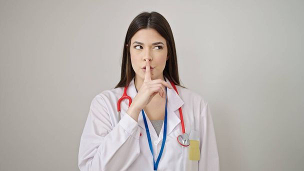 Νεαρή όμορφη Ισπανίδα γιατρός ζητάει ησυχία σε απομονωμένο λευκό φόντο. - Φωτογραφία, εικόνα