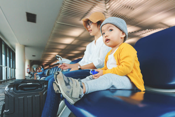 Cute Asian Chinese mother and her Little child son waiting for a flight at international airport terminal together. Travel Holiday, Vacation concept. - Фото, зображення