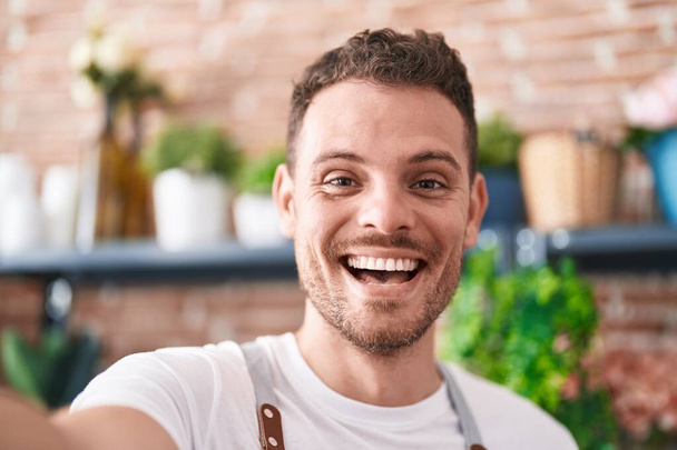 Молодий іспаномовний чоловік флорист посміхається впевнено зробити селфі на камеру у флориста
 - Фото, зображення