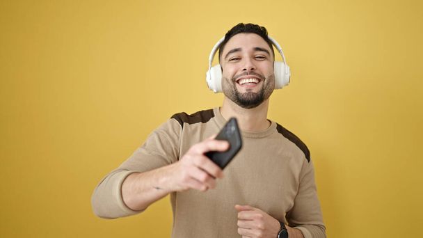 Fiatal arab férfi mosolygós magabiztos hallgat zenét és táncol izolált sárga háttér - Fotó, kép