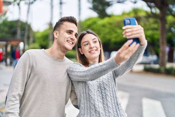 Мужчина и женщина обнимают друг друга делают селфи с помощью смартфона на улице - Фото, изображение