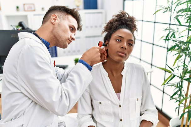 Man and woman wearing doctor uniform examining ear using otoscope at clinic - Zdjęcie, obraz