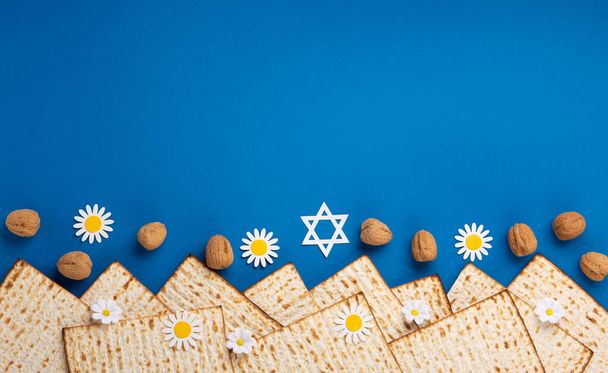 ユダヤ人の休日マツァ、ナッツ、青いテーブルの春の花と過越の挨拶カードの概念。Seder Pesach春休みの背景、トップビュー、コピースペース. - 写真・画像