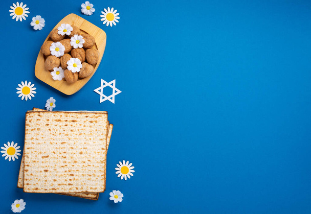 Jewish holiday Passover greeting card concept with matzah, nuts, spring flowers on blue table. Seder Pesach spring holiday background, top view, copy space. - Photo, Image
